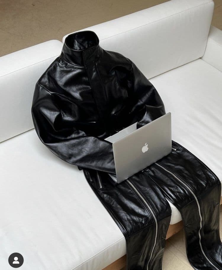 A black leather jacket draped over a white sofa, with an open laptop resting on it